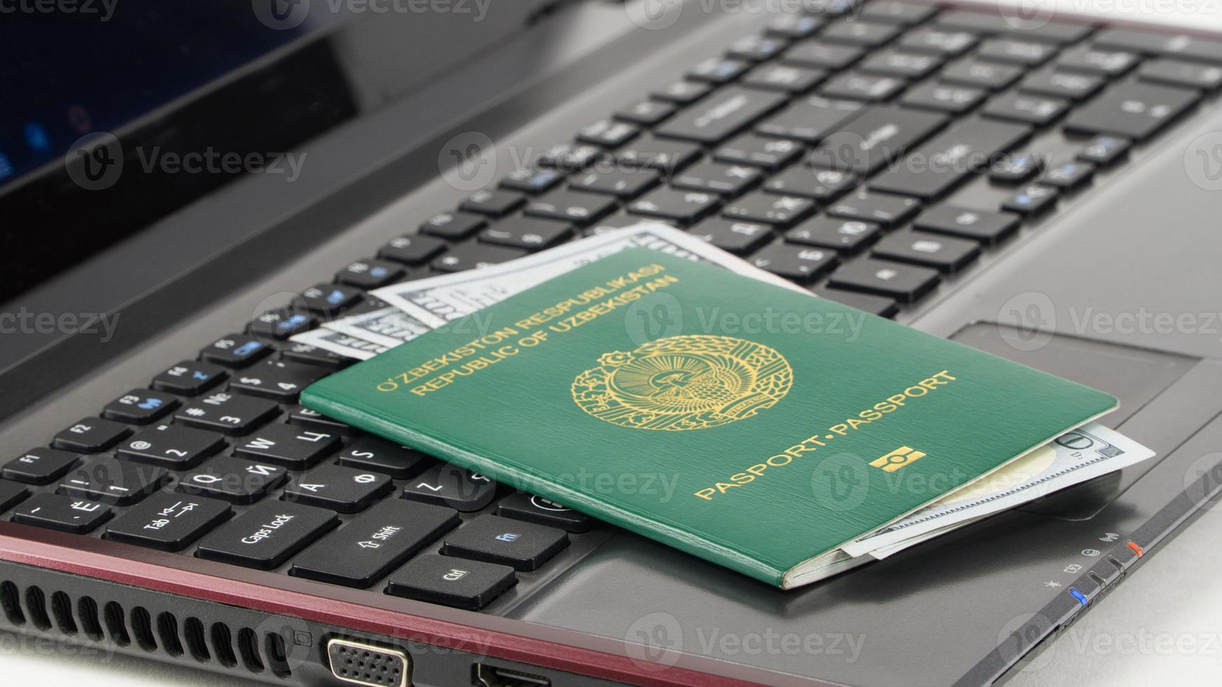 passaporto dell'Uzbekistan con noi dollari sulla tastiera del laptop. registrazione online. concetto - corruttore e corruzione foto