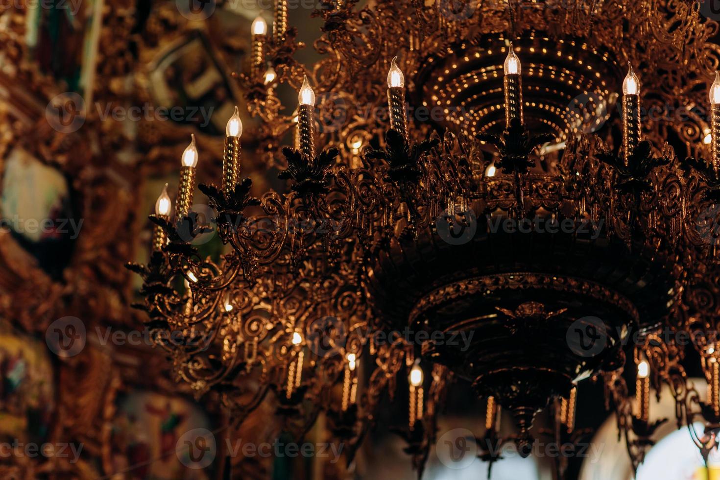 un lampadario placcato in oro è appeso nella vecchia chiesa vicino alle icone. le lampade moderne sono come candele. foto