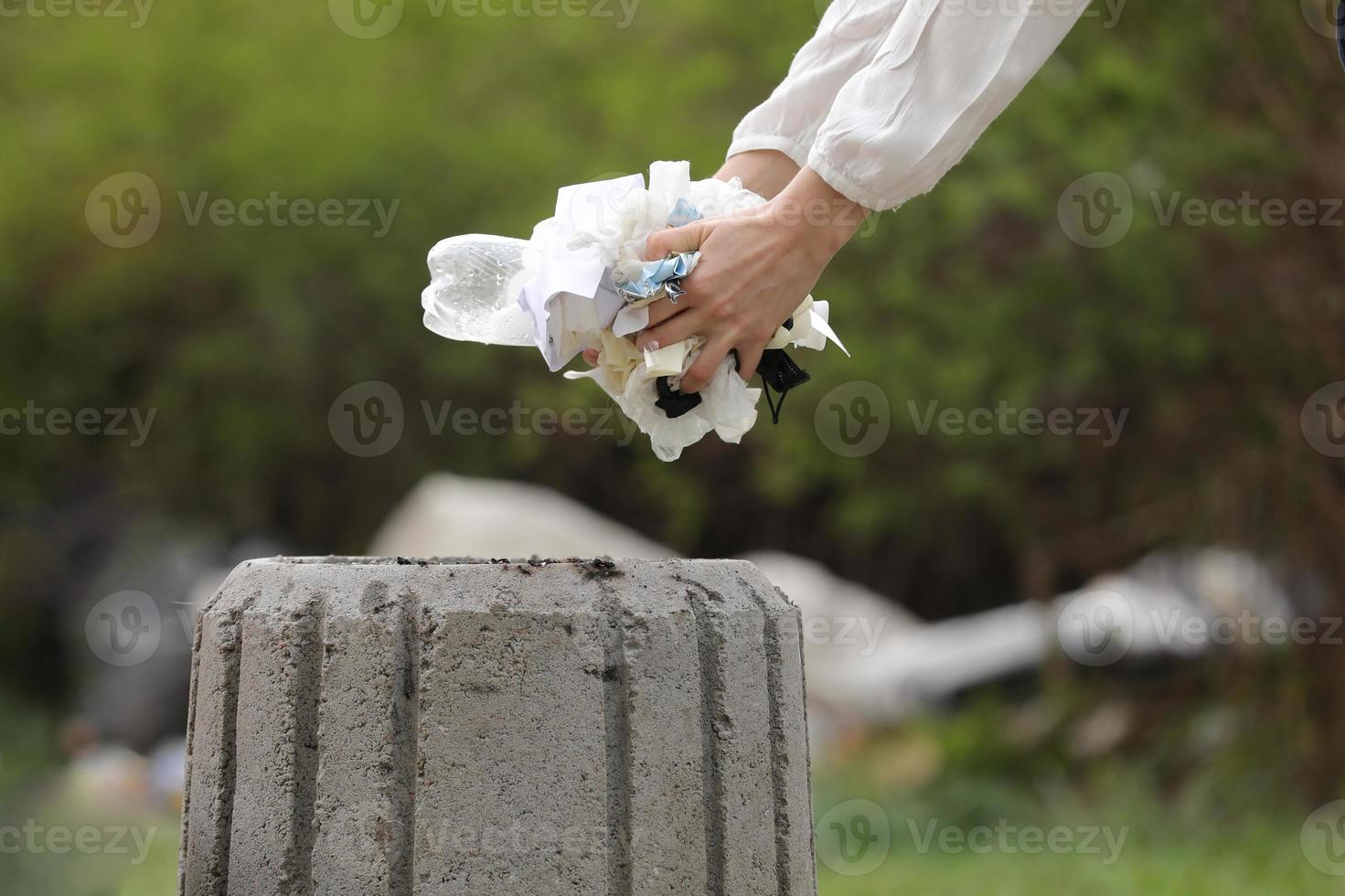 donna getta spazzatura di plastica nella spazzatura. mano della donna che raccoglie la plastica dell'immondizia per la pulizia al parco. raccolta dei rifiuti dopo una pandemia. messa a fuoco selettiva foto