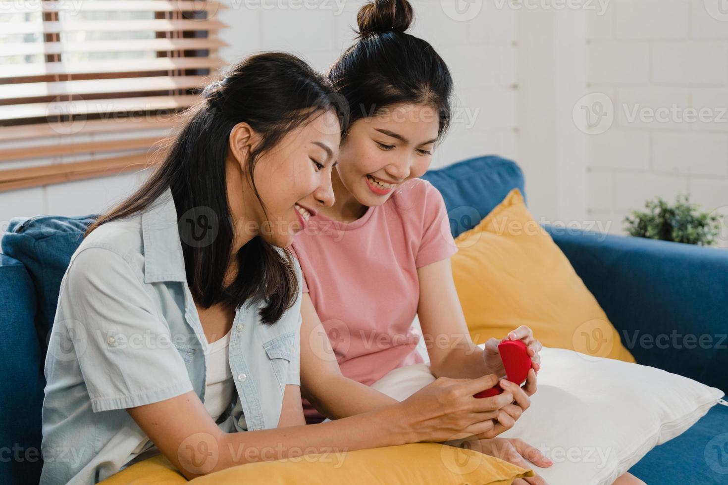 le coppie di donne lesbiche asiatiche lgbtq si propongono a casa, la giovane amante asiatica sorride felice ha del tempo romantico mentre propone e il matrimonio a sorpresa indossa la fede nuziale nel soggiorno a casa concetto. foto