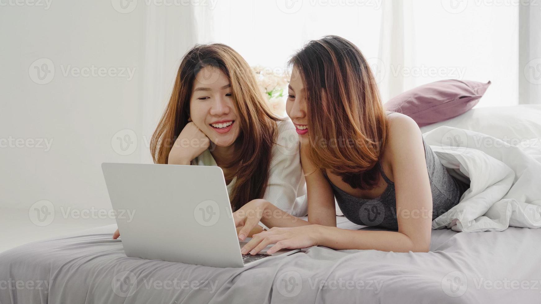 belle giovani donne asiatiche lgbt lesbica coppia felice seduta sul letto abbraccio e utilizzando il computer portatile insieme camera da letto a casa. lgbt coppia lesbica insieme al chiuso concetto. passare del tempo piacevole a casa. foto