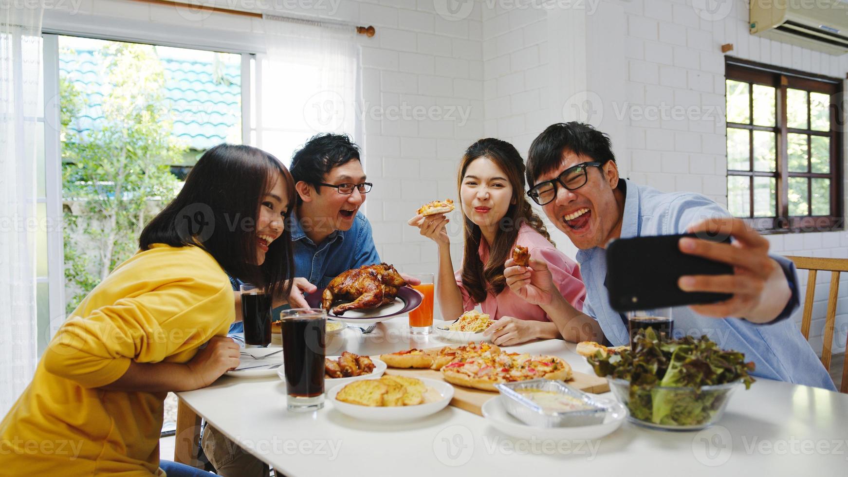 giovane gruppo felice che pranza a casa. festa di famiglia asiatica mangiando pizza e facendo selfie con i suoi amici alla festa di compleanno al tavolo da pranzo insieme a casa. festa di celebrazione e stare insieme foto