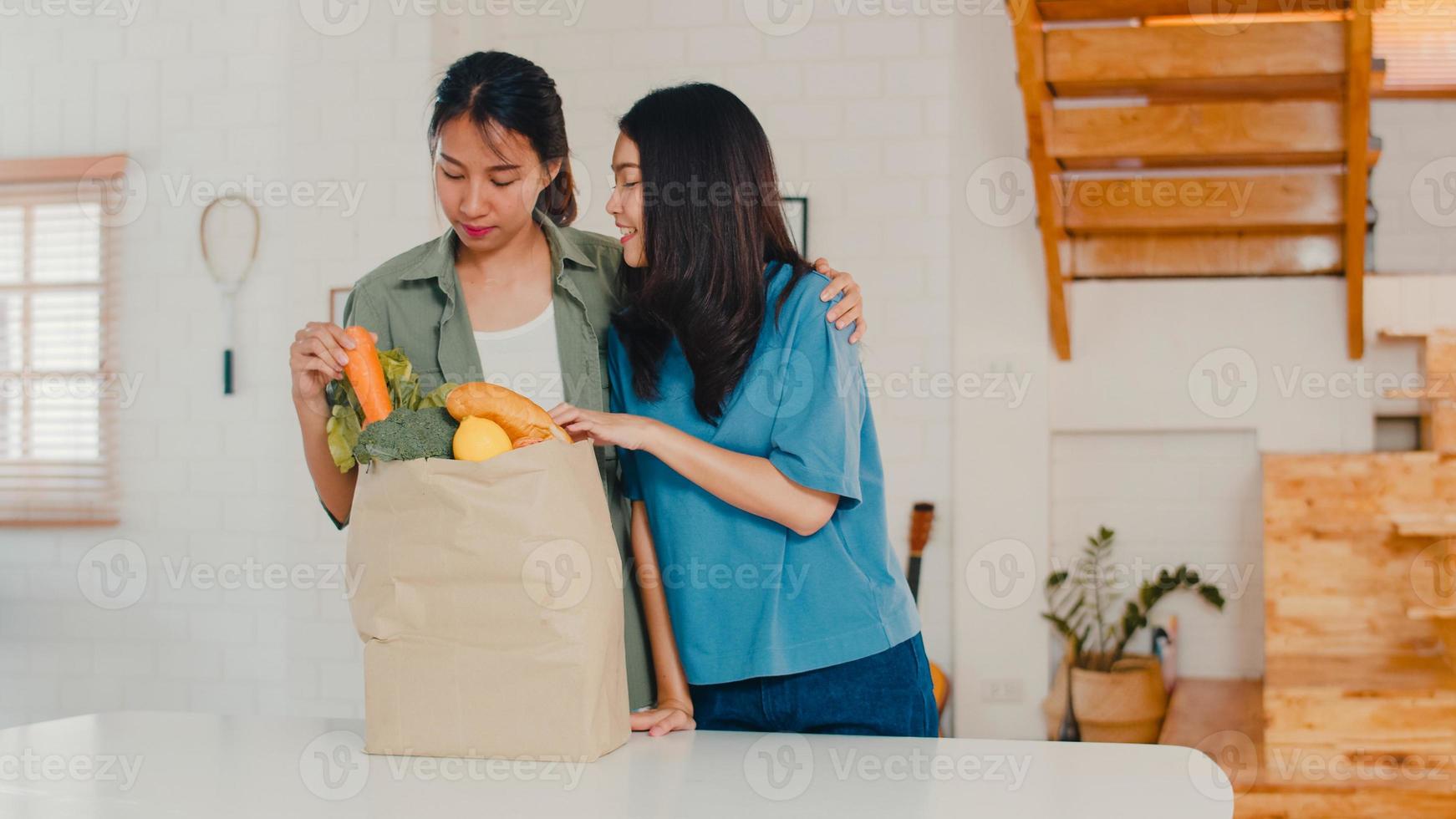 Le coppie di donne lesbiche asiatiche lgbtq tengono i sacchetti di carta della spesa a casa, la giovane ragazza asiatica felice compra le verdure e il prodotto sano della frutta dal supermercato lo mettono in cucina il concetto di mattina. foto