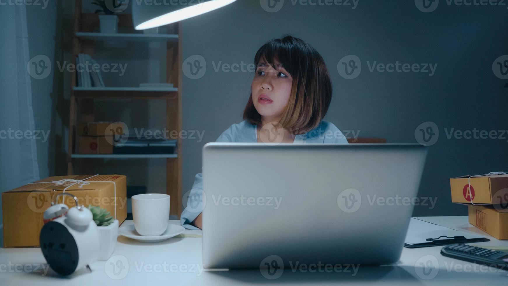 giovane imprenditore asiatico donna d'affari proprietaria di PMI online controllando il prodotto in magazzino e salvando sul laptop che lavora di notte a casa. sentirsi male e stanco. piccolo imprenditore al concetto di home office. foto