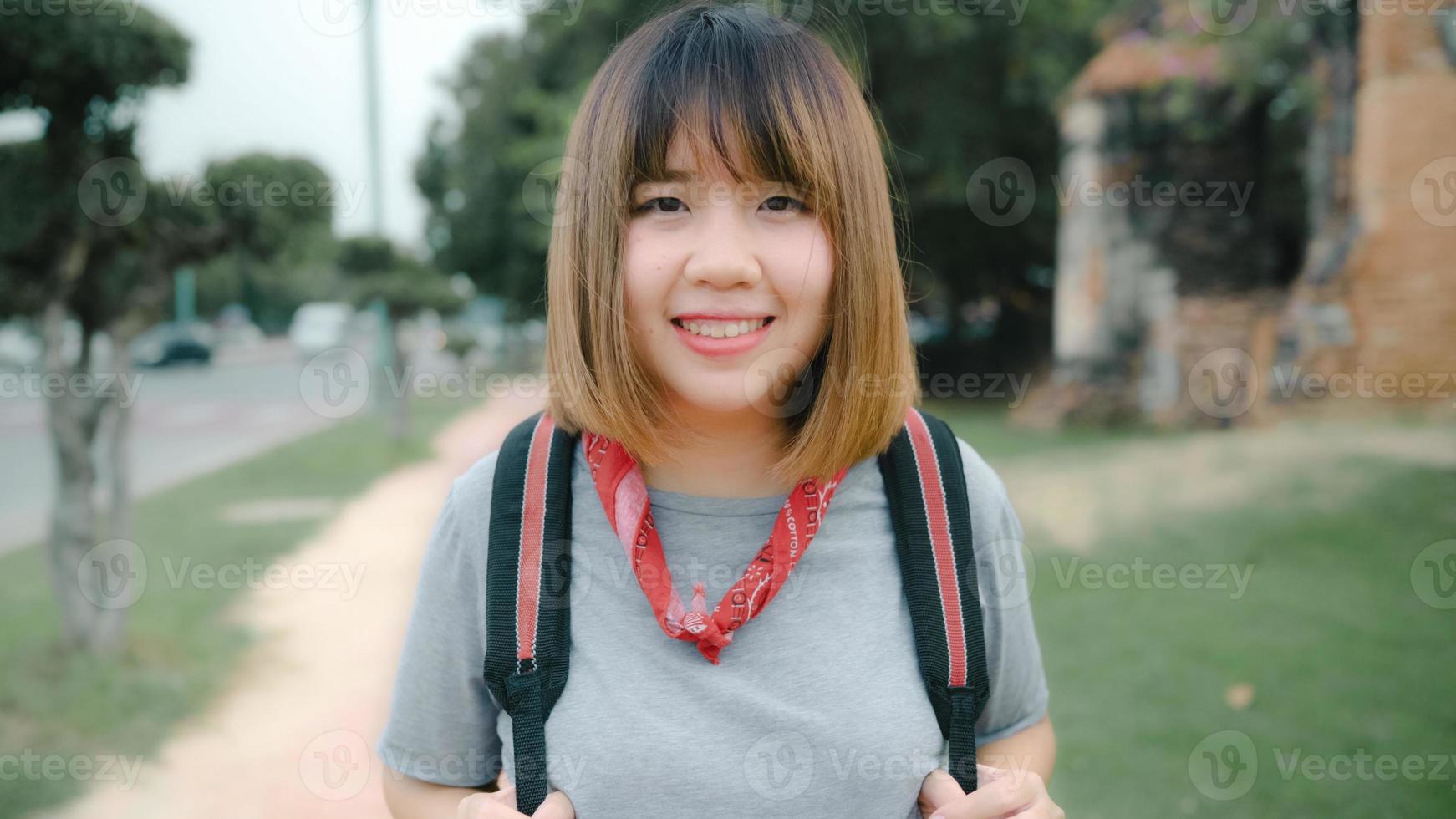 la donna asiatica del viaggiatore che si sente felice sorridendo alla macchina fotografica del viaggio di vacanza ad ayutthaya, in tailandia, la femmina del viaggiatore con zaino e sacco a pelo si gode il suo viaggio in un punto di riferimento straordinario nella città tradizionale. concetto di vacanze di viaggio di stile di vita foto