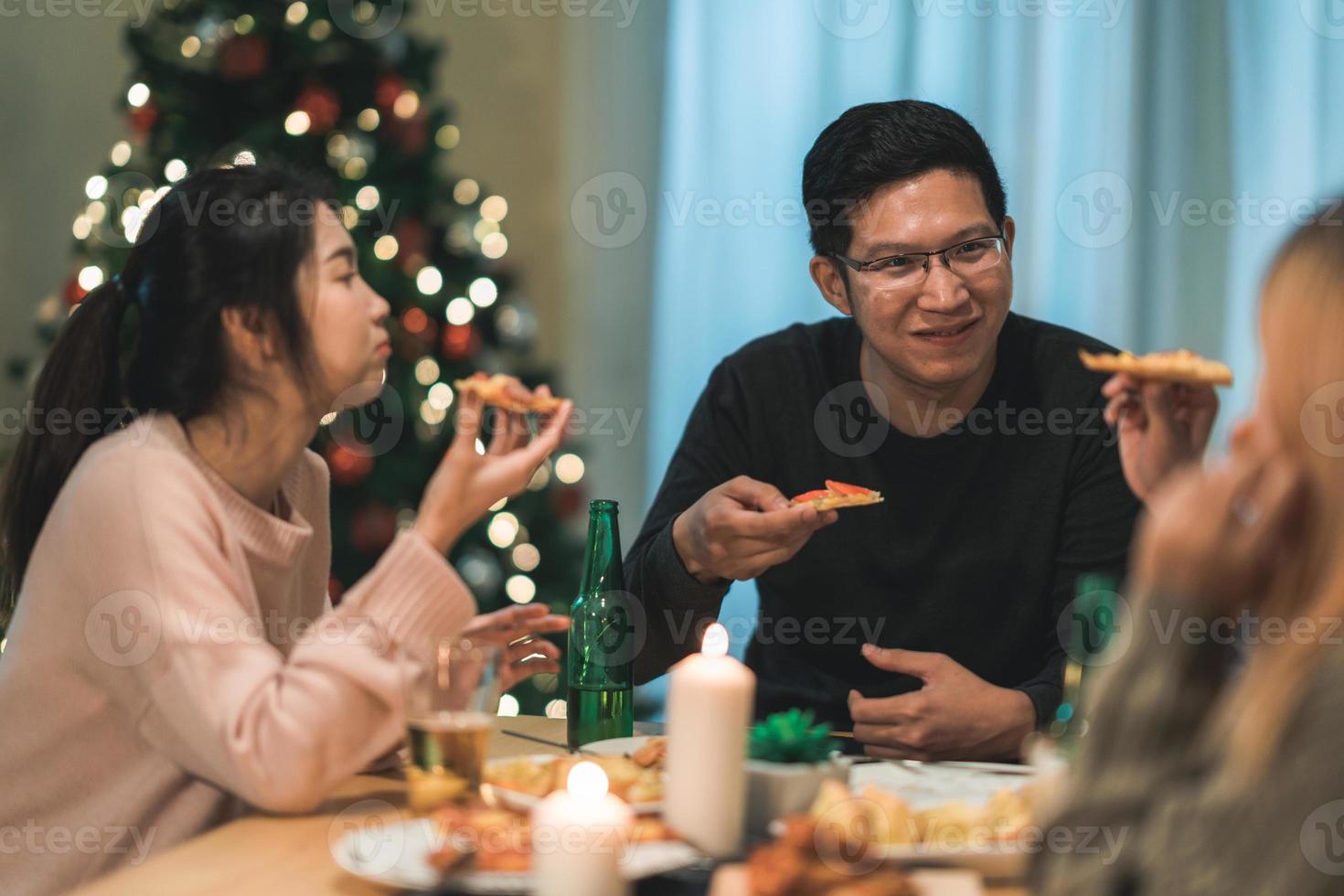 buon natale e felice anno nuovo gruppo di giovani amici a cena a casa. festa di famiglia asiatica con birra e pizza vicino all'albero di natale a casa di notte. festa di celebrazione e stare insieme. foto
