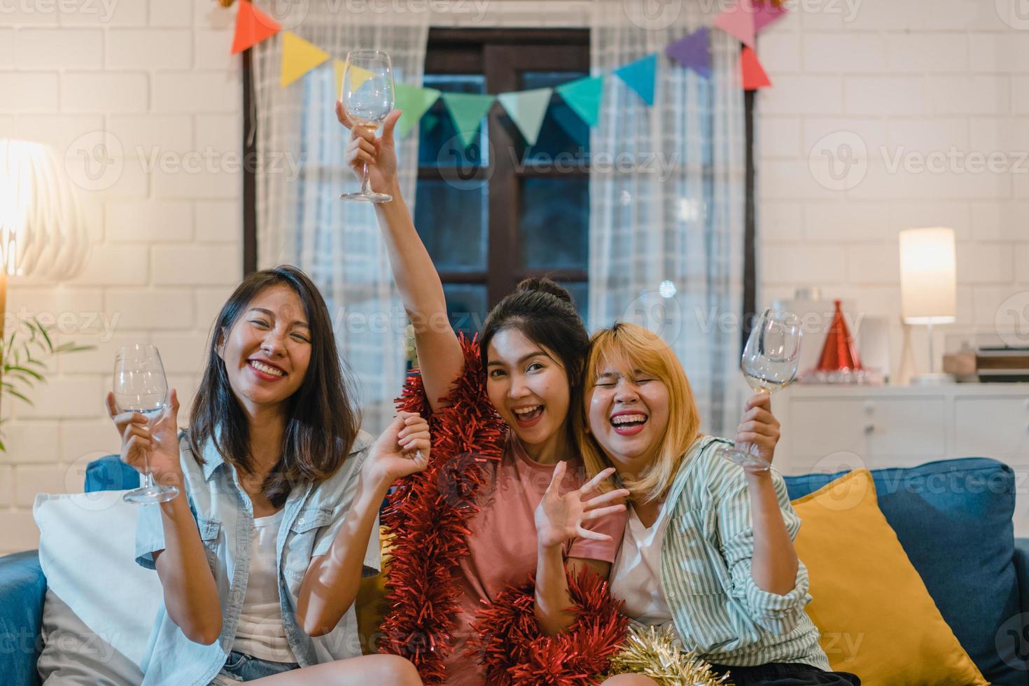 gruppo di donne asiatiche festa a casa, cocktail femminile che parla divertendosi insieme sul divano nel soggiorno di notte. adolescente giovane amico gioca, amicizia, celebra il concetto di vacanza. foto