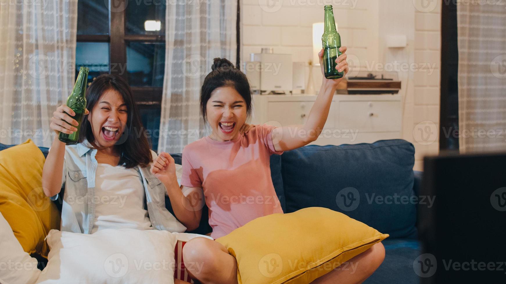 donne lesbiche lgbt coppia festa a casa, donna asiatica che beve birra guardando la tv tifo calcio momento divertente insieme sul divano nel soggiorno di notte. giovane tifoso amante del calcio, celebra il concetto di vacanza. foto