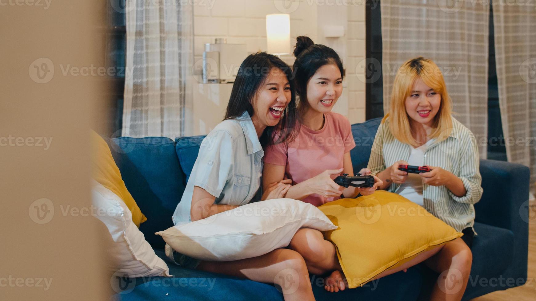 un gruppo di coppie di donne asiatiche gioca a casa, donne che usano il joystick che hanno momenti divertenti insieme sul divano nel soggiorno di notte. adolescente giovane amico tifoso di calcio, celebra il concetto di vacanza. foto