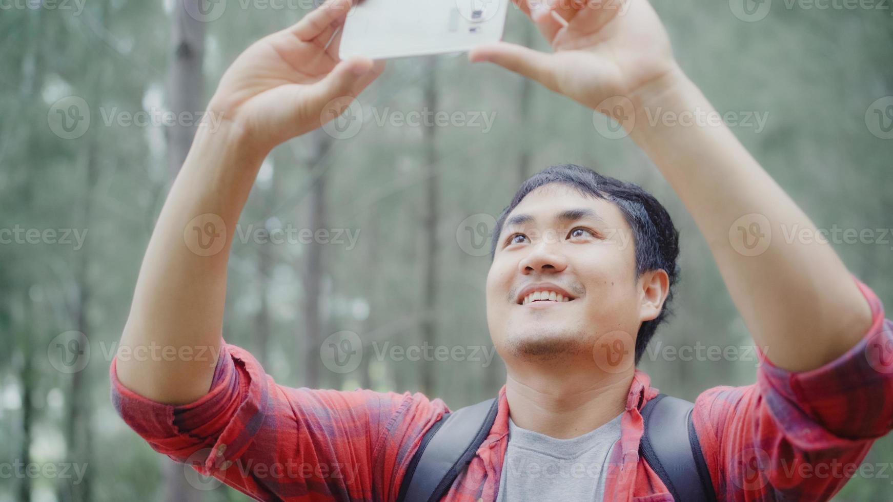 escursionista asia zaino in spalla uomo che usa lo smartphone per scattare una foto mentre è in avventura escursionistica camminando nella foresta, il maschio asiatico si gode le vacanze vicino a un sacco di alberi. stile di vita gli uomini viaggiano e si rilassano concetto.