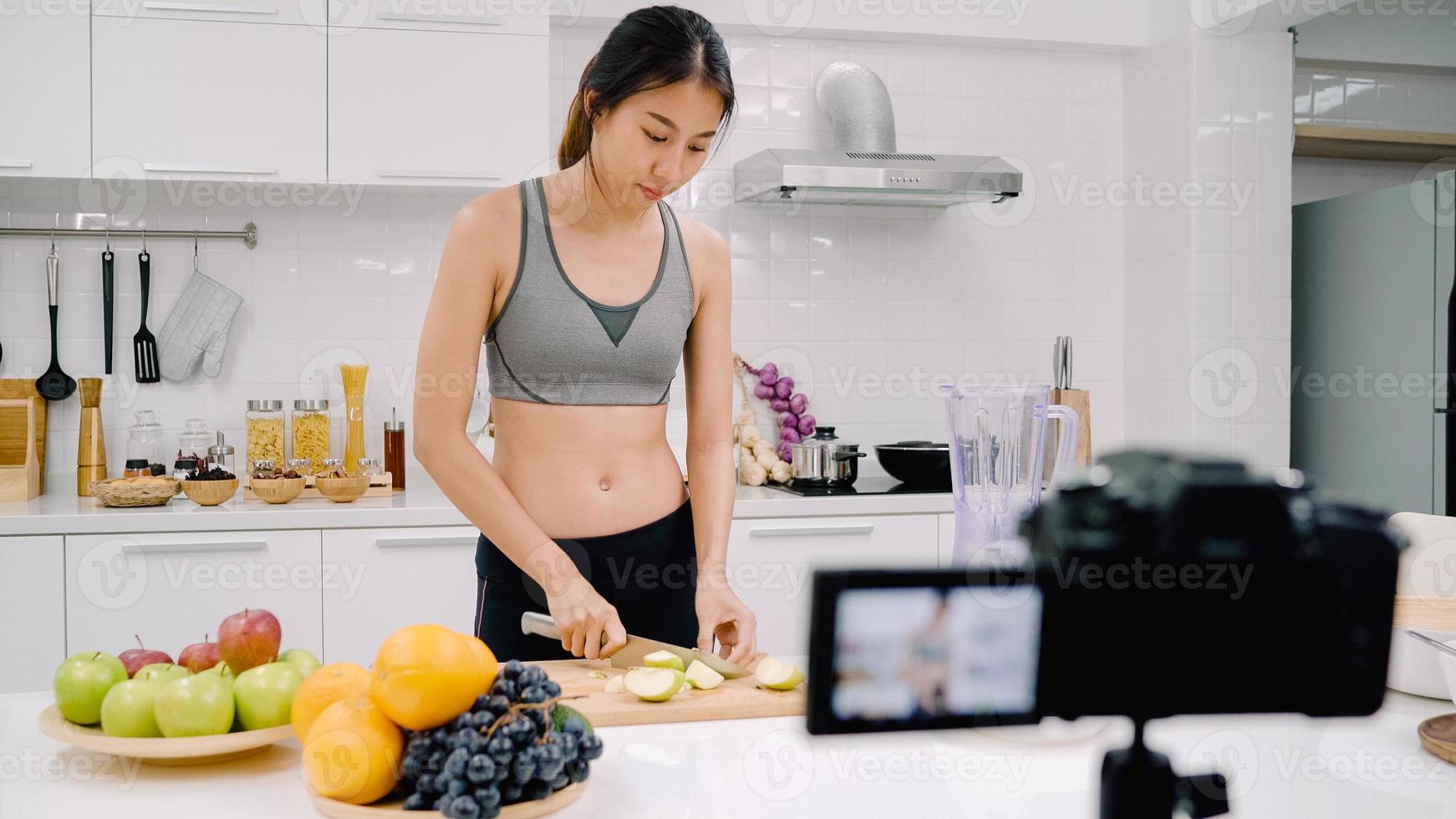 blogger sportiva donna asiatica che utilizza la videocamera che registra come fare il video del succo di mela per il suo abbonato, le donne usano frutta biologica che fa il succo di mela da sola a casa. concetto di cibo sano. foto