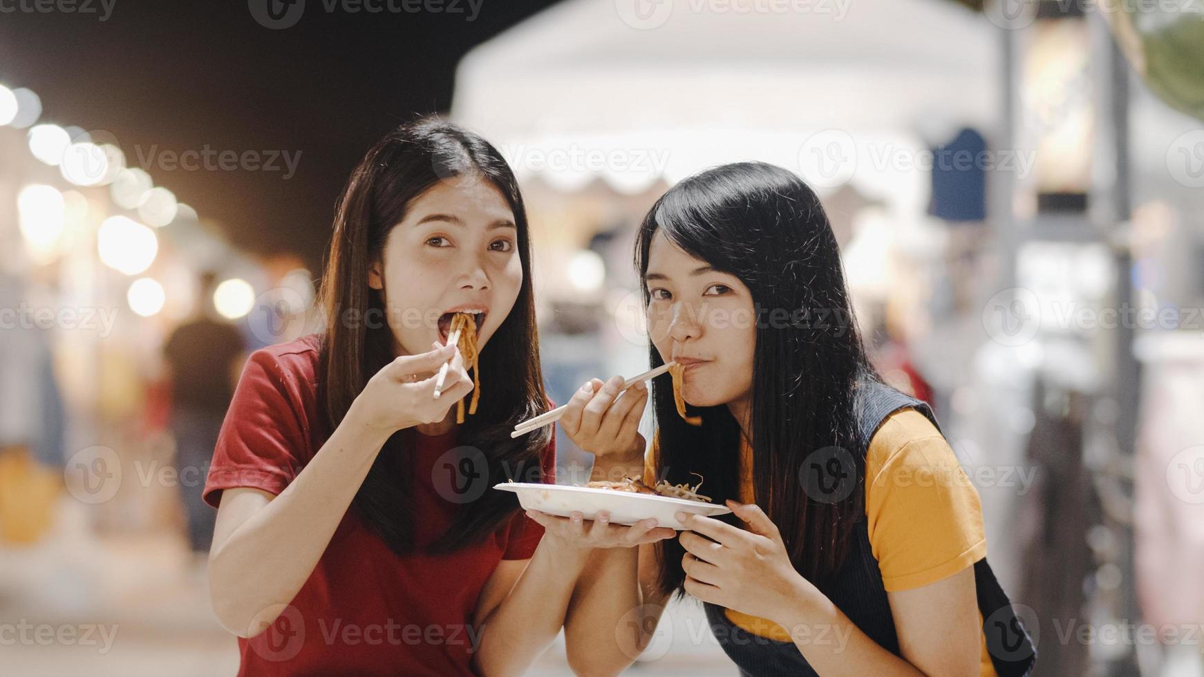 gli amici delle giovani donne asiatiche viaggiano a bangkok, in tailandia, bella donna che si sente felice camminando e mangiando pad thai sulla strada di khao san. le donne viaggiano mangiano cibo di strada nel concetto di thailandia. foto