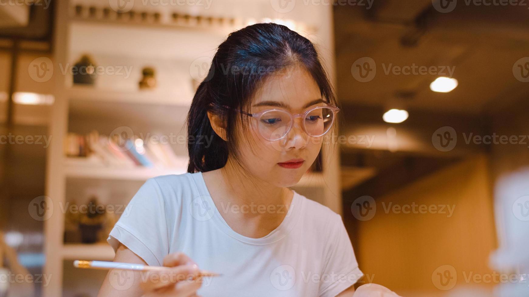 studentesse asiatiche che leggono libri in biblioteca all'università. giovane studentessa universitaria fa i compiti, legge libri di testo, studia duramente per la conoscenza sulla scrivania della notte degli straordinari del campus universitario. foto