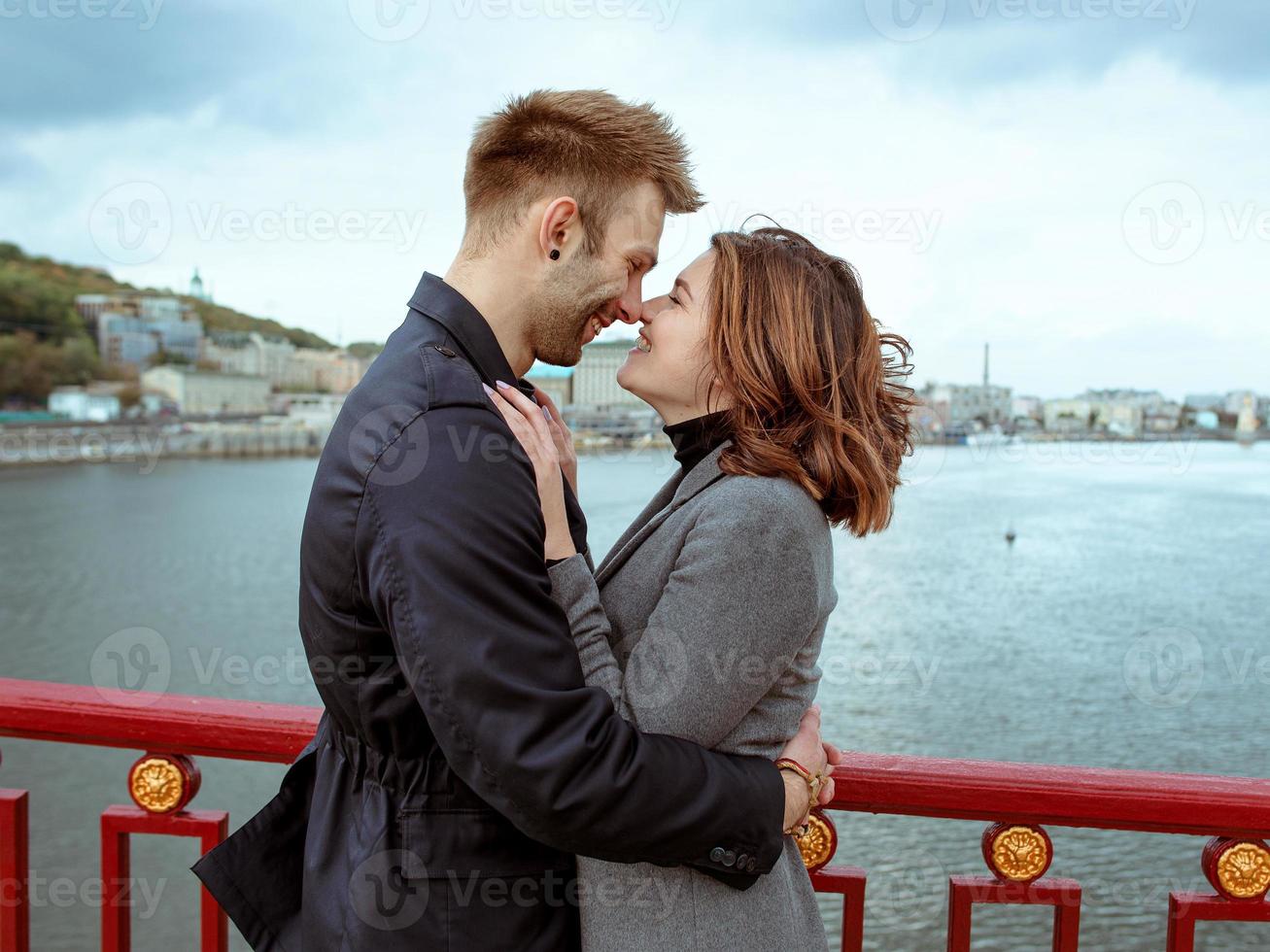 bella incredibile divertente allegra giovane coppia che si abbraccia all'aperto vicino al fiume sullo sfondo del ponte. fidanzata e fidanzato. concetto di famiglia, amore e amicizia foto