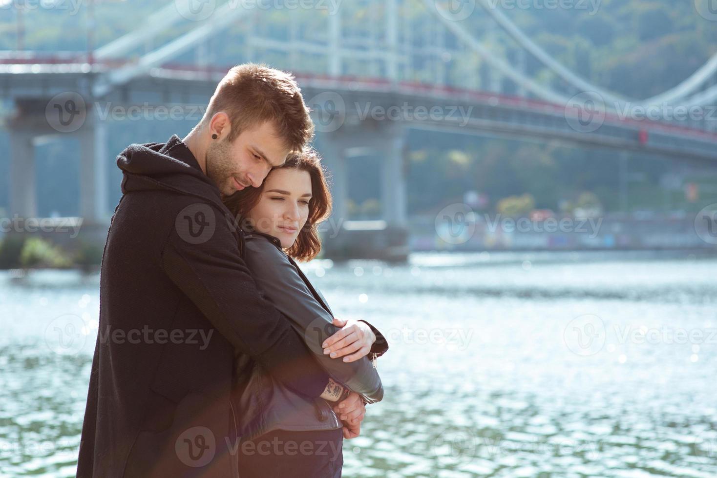 bella incredibile divertente allegra giovane coppia che si abbraccia all'aperto vicino al fiume sullo sfondo del ponte. fidanzata e fidanzato. concetto di famiglia, amore e amicizia foto