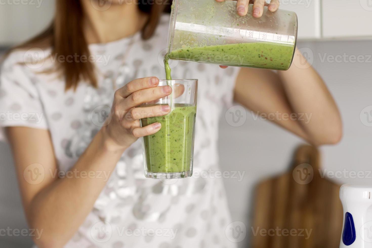 bella ragazza beve frullato appena preparato in cucina. frullati appena fatti con ingredienti vegetali assortiti sul bancone della cucina. mangiare sano. messa a fuoco selettiva foto