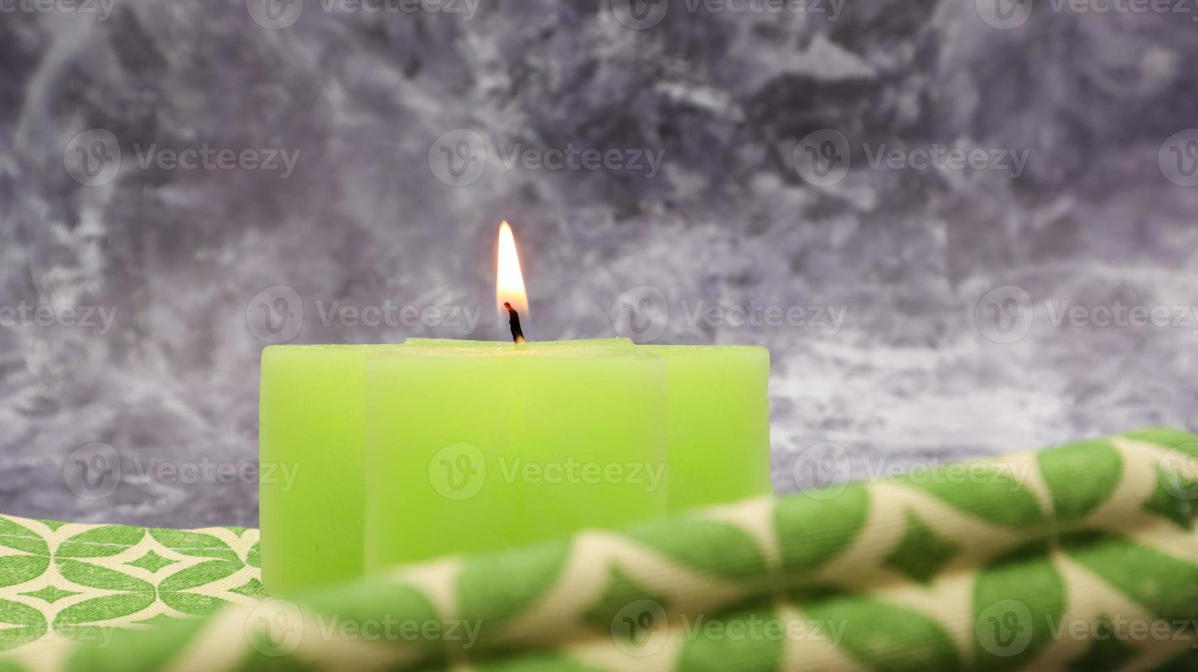 composizione con una candela accesa di verde su un tavolo con un tovagliolo di lino verde su un bellissimo sfondo di marmo grigio. posto per il tuo testo. decorazioni natalizie. foto