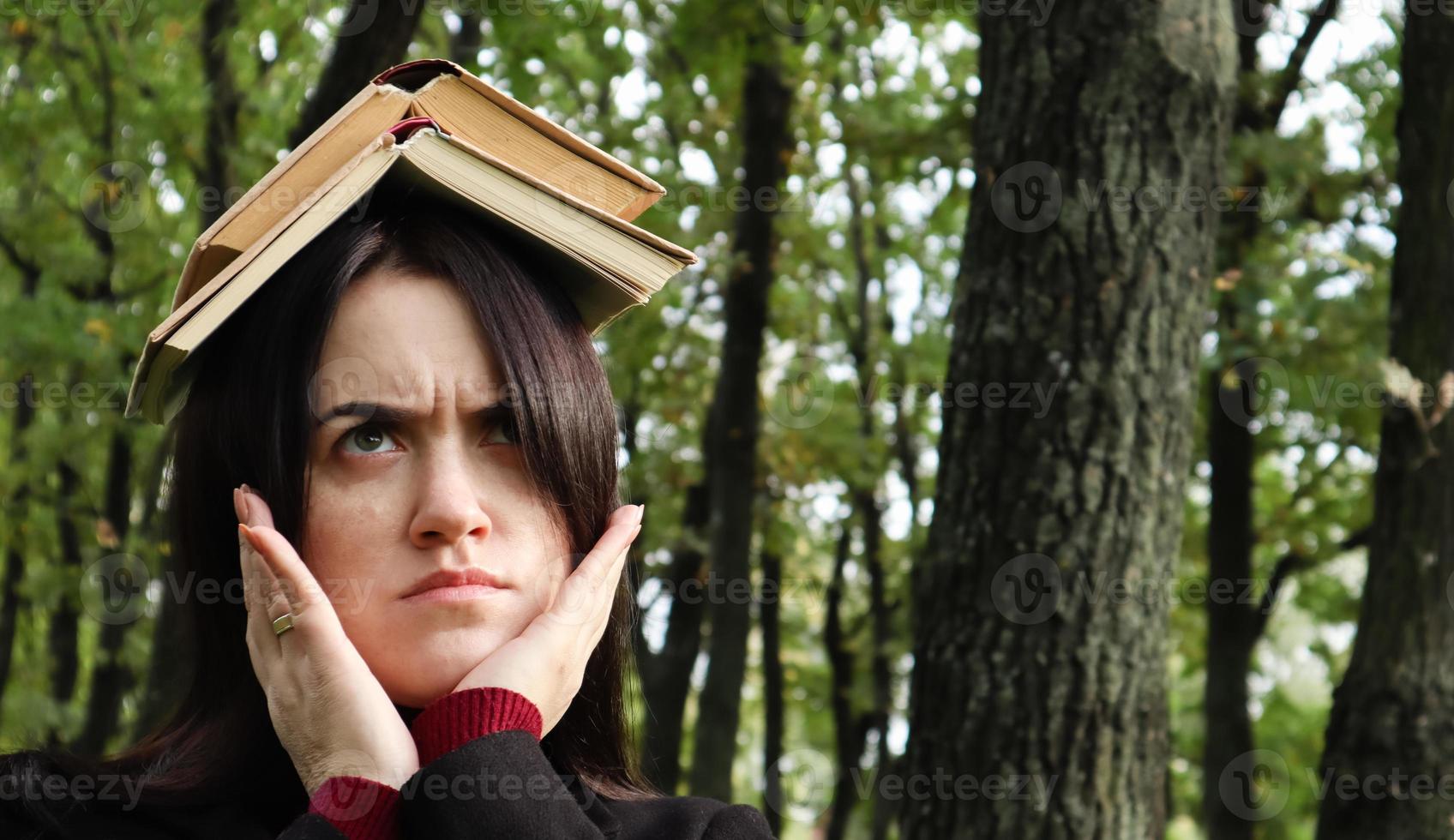 ritratto di una giovane e divertente bruna nel parco con in mano un libro aperto sulla testa. l'apprendimento è divertente. donna in equilibrio con i libri sulla testa. lo studente è stanco di leggere. foto