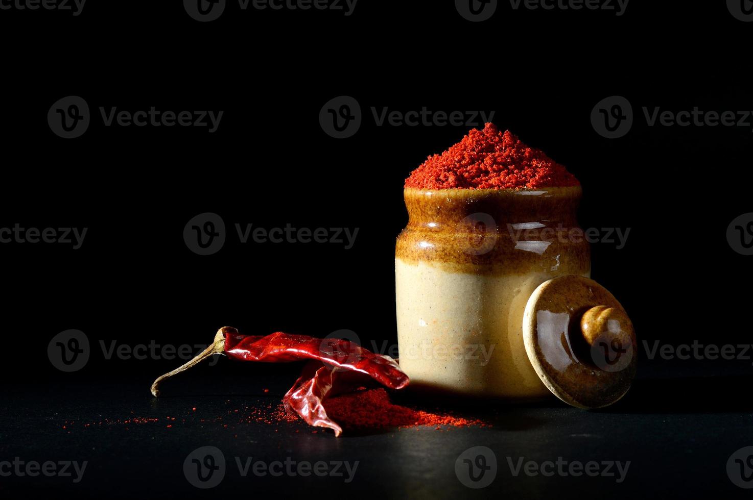 Peperoncino rosso in polvere in vaso di argilla con peperoncino rosso su sfondo nero foto