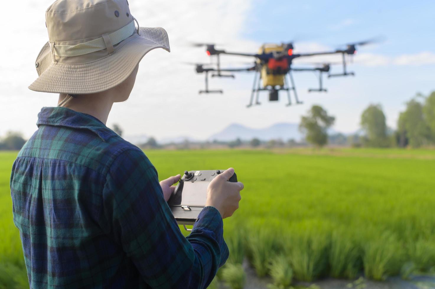 giovane agricoltore intelligente che controlla i droni che spruzzano fertilizzanti e pesticidi su terreni agricoli, innovazioni ad alta tecnologia e agricoltura intelligente foto