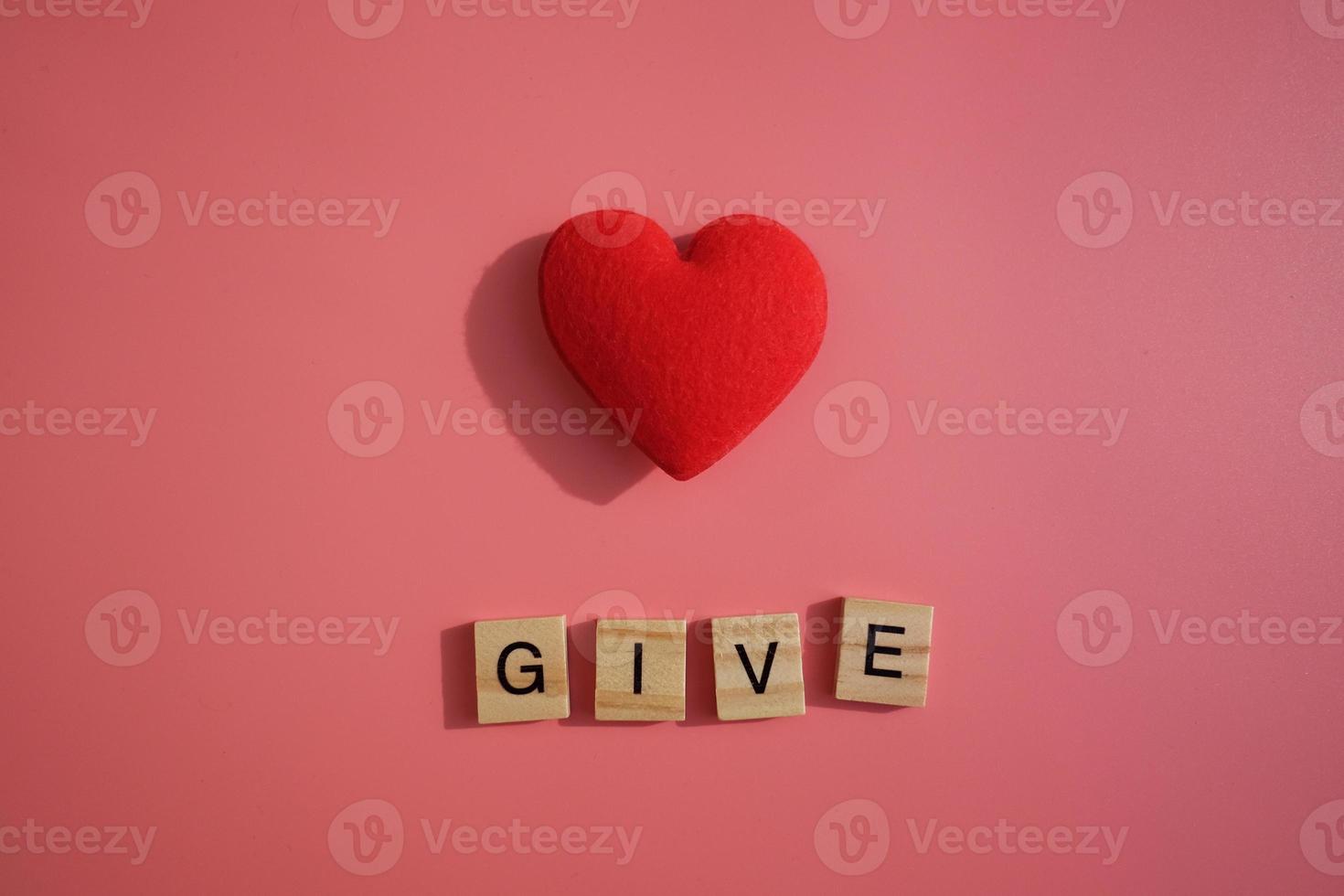 cuore rosso con lettere di parole di dare isolato su sfondo rosa. dare, condividere, enti di beneficenza e donare concetto. foto