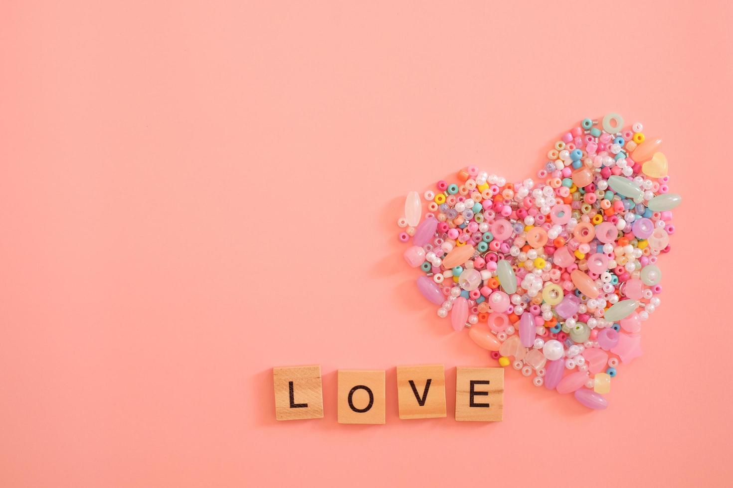 a forma di cuore colorato fatto di perline come simbolo d'amore con lettere d'amore isolate su sfondo rosa chiaro pastello. san valentino, regalo, messaggio dell'amante, biglietto di auguri. concetto di amore. foto