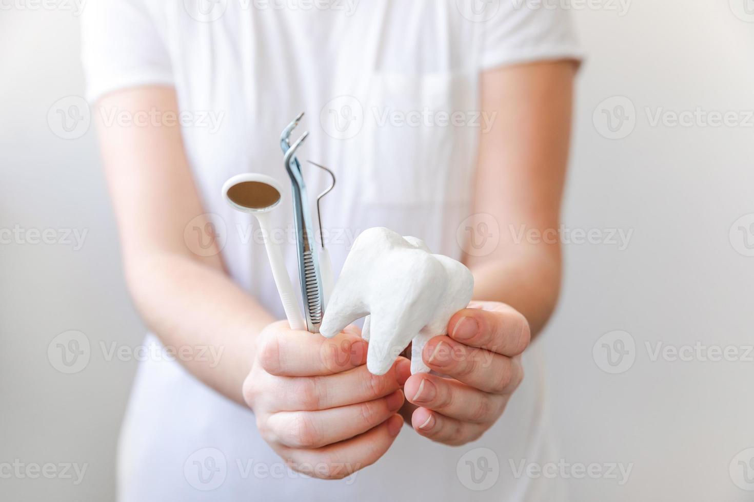 concetto di cure odontoiatriche. mano della donna che tiene il modello di dente sano bianco e gli strumenti del dentista dentale isolati su sfondo bianco. sbiancamento dei denti, igiene orale dentale, restauro dei denti, giornata del dentista. foto