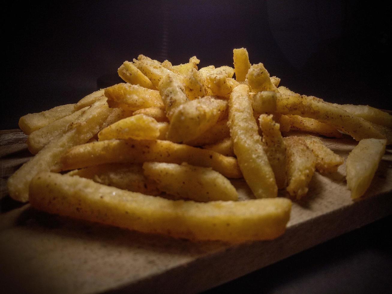 foto ravvicinata di patatine fritte su un tagliere di legno, con sfondo nero.