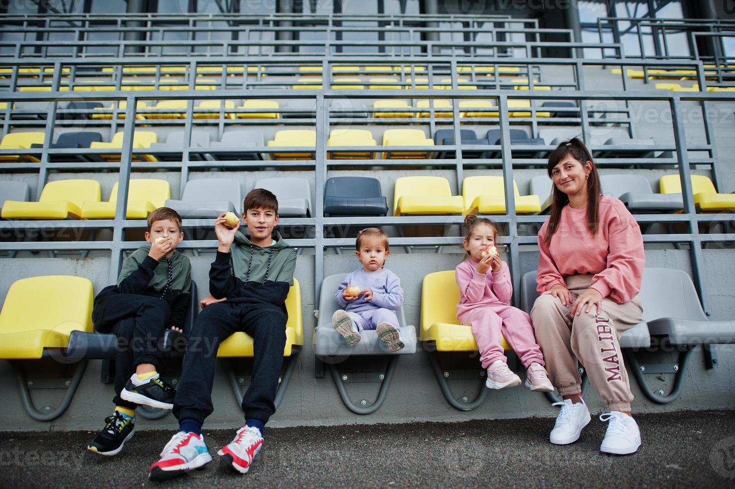 giovane madre alla moda con quattro bambini seduti su sedie allo stadio. la famiglia trascorre il tempo libero all'aperto. foto