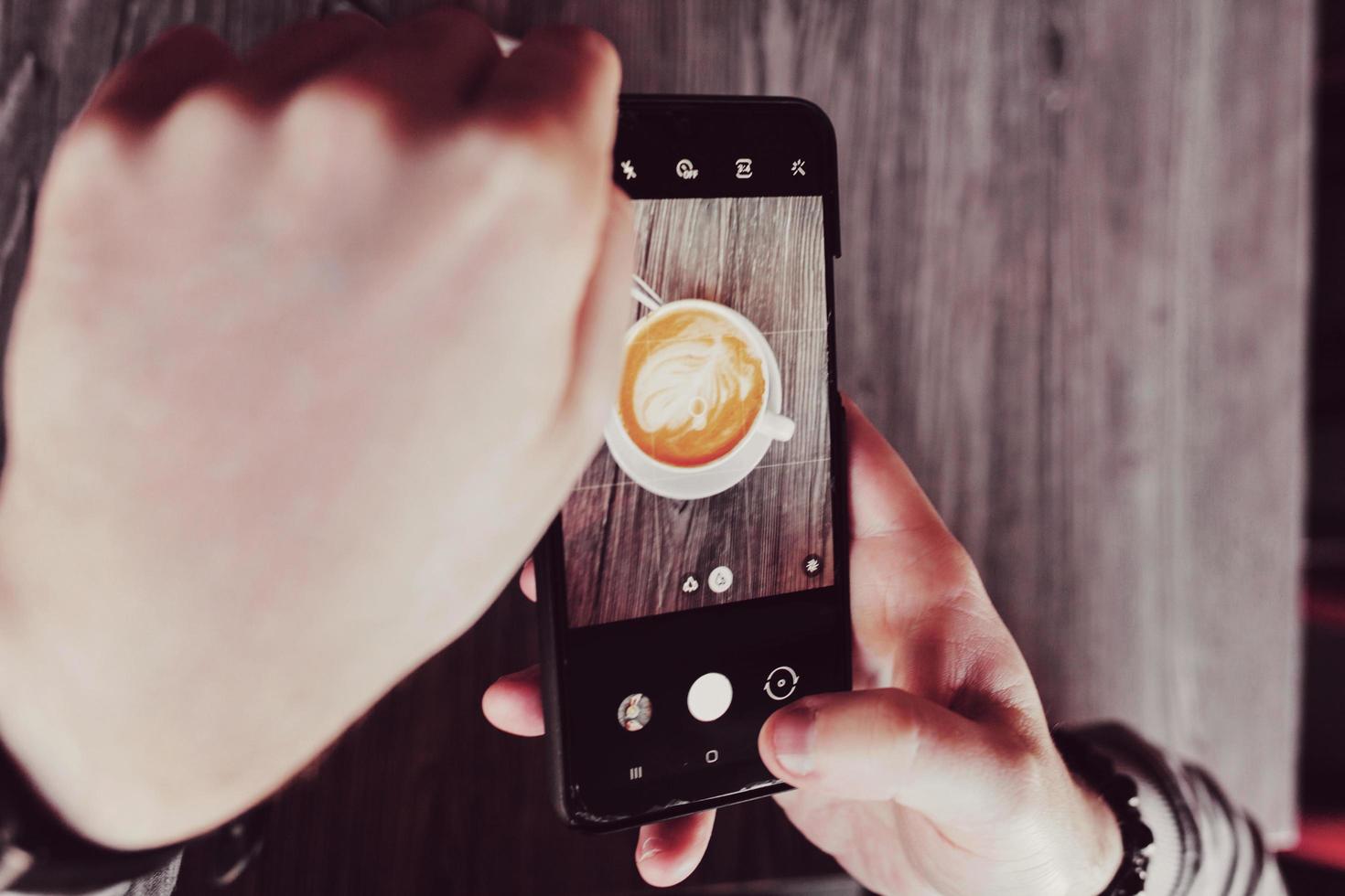 le mani tengono un telefono e una tazza di caffè foto