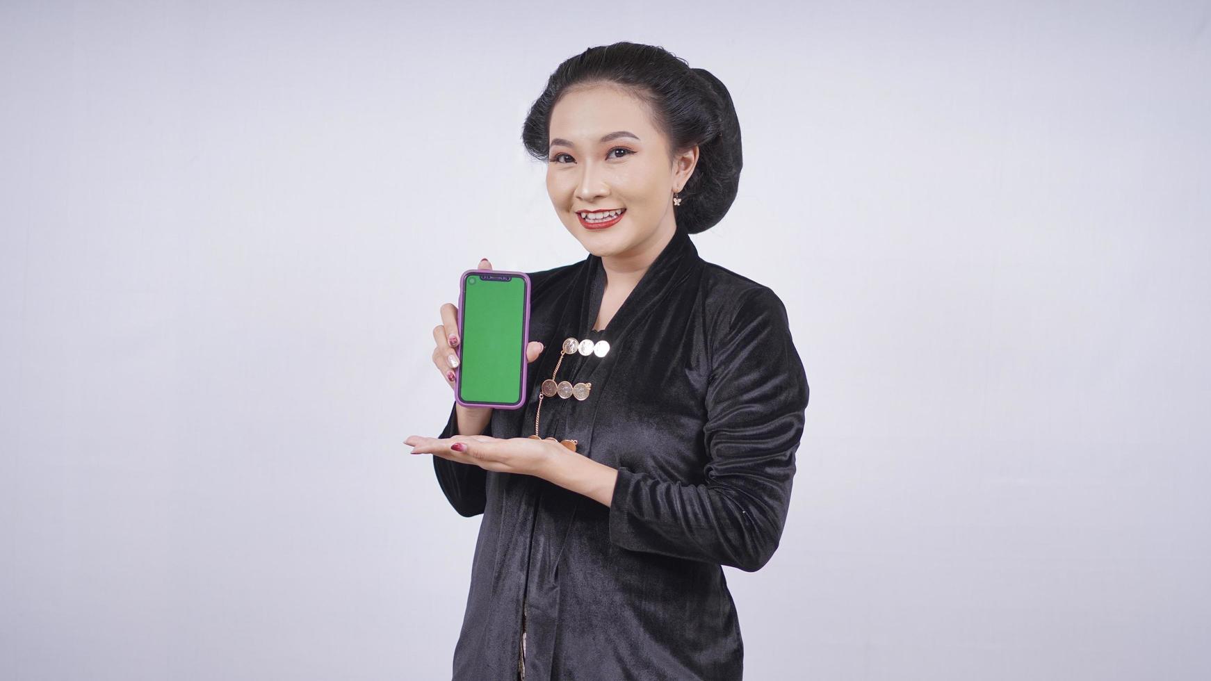 bellezza asiatica in kebaya che mostra lo schermo dello smartphone isolato su sfondo bianco foto