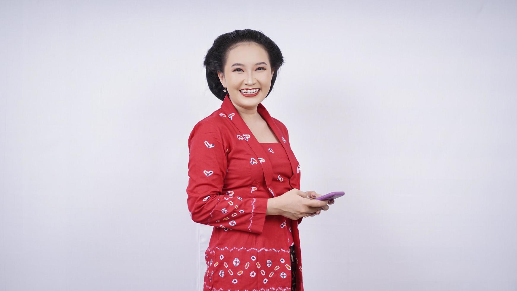 bellezza asiatica in kebaya ridacchia con lo smartphone isolato su sfondo bianco foto