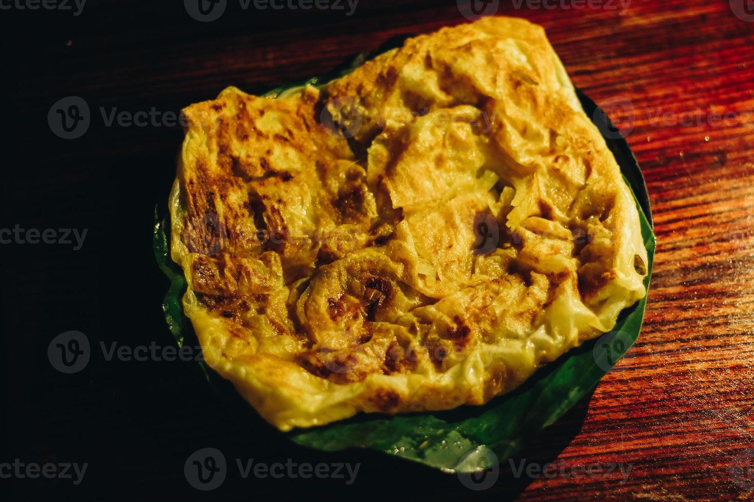roti canai o pane canai o pane parata o pane prata con salsa al curry sul piatto di foglie di banana isolato su fondo di legno con fondo scuro e riflettori foto