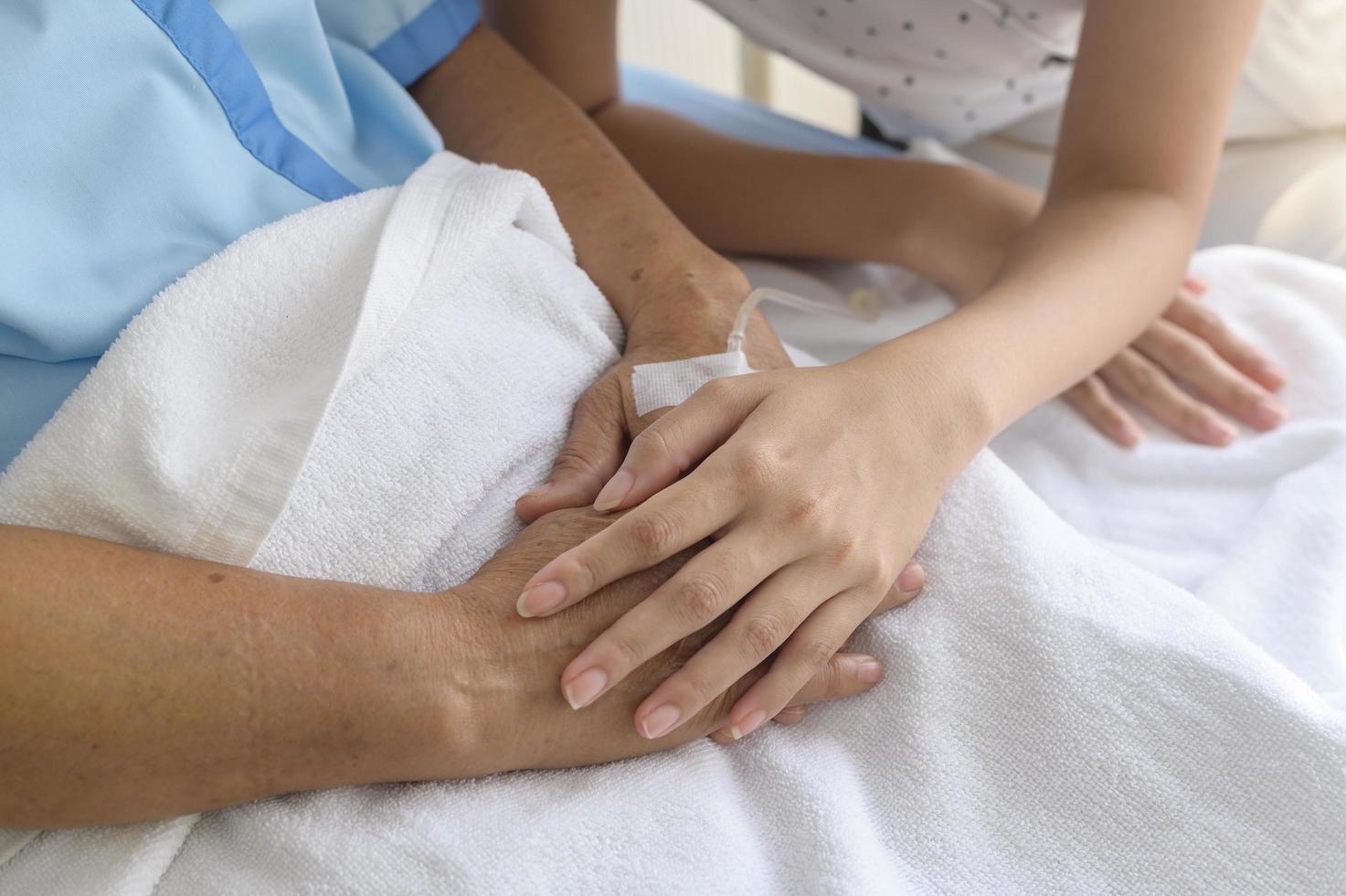 primo piano del visitatore che tiene la mano del paziente anziano in ospedale, assistenza sanitaria e concetto medico foto