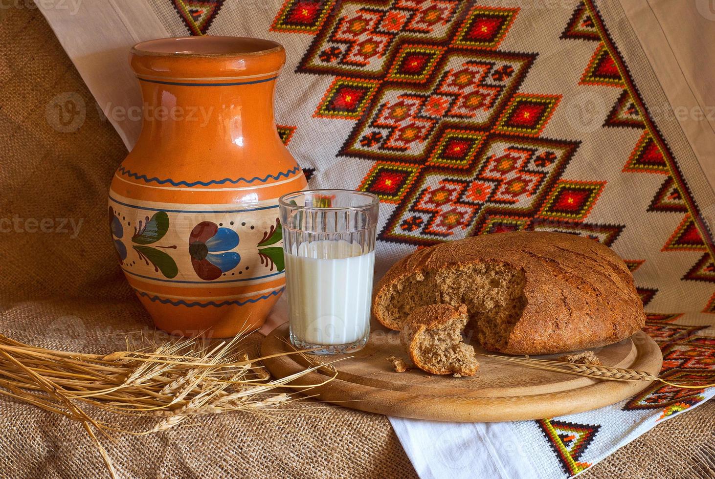 natura morta con una brocca di pane bicchiere di spighe di latte e asciugamano nazionale ucraino fatto a mano con ricamo foto