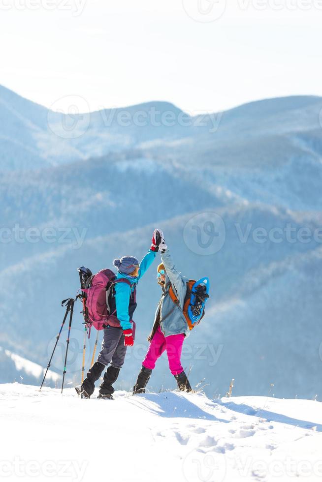 due donne sono salite in cima alla montagna durante un'escursione invernale, la ragazza dà il cinque a un'amica foto