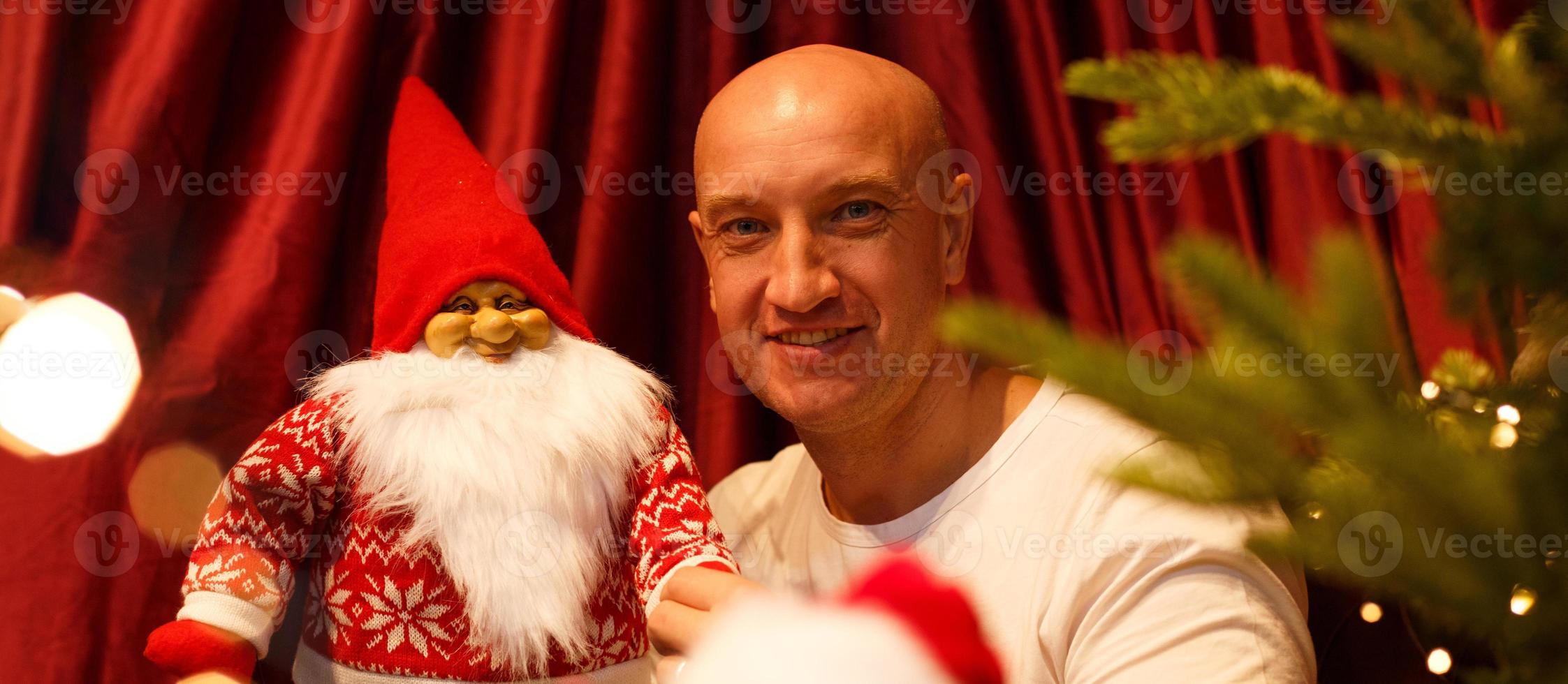 ritratto di un uomo calvo che tiene un giocattolo di babbo natale all'albero di natale foto