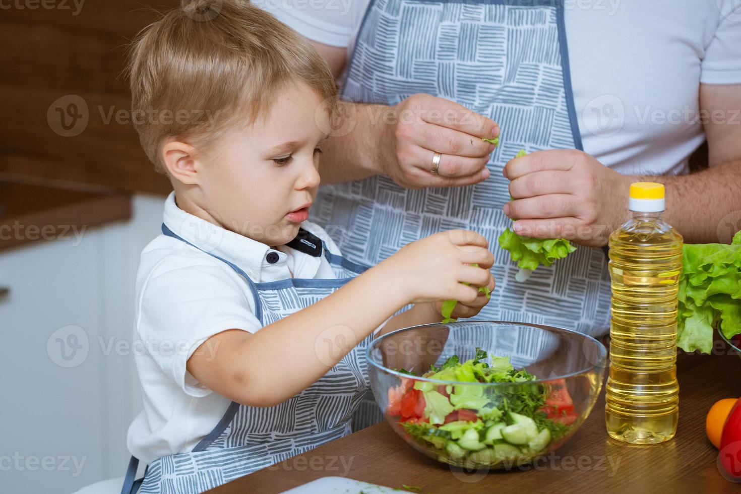 figlio e padre preparano insieme l'insalata in cucina foto