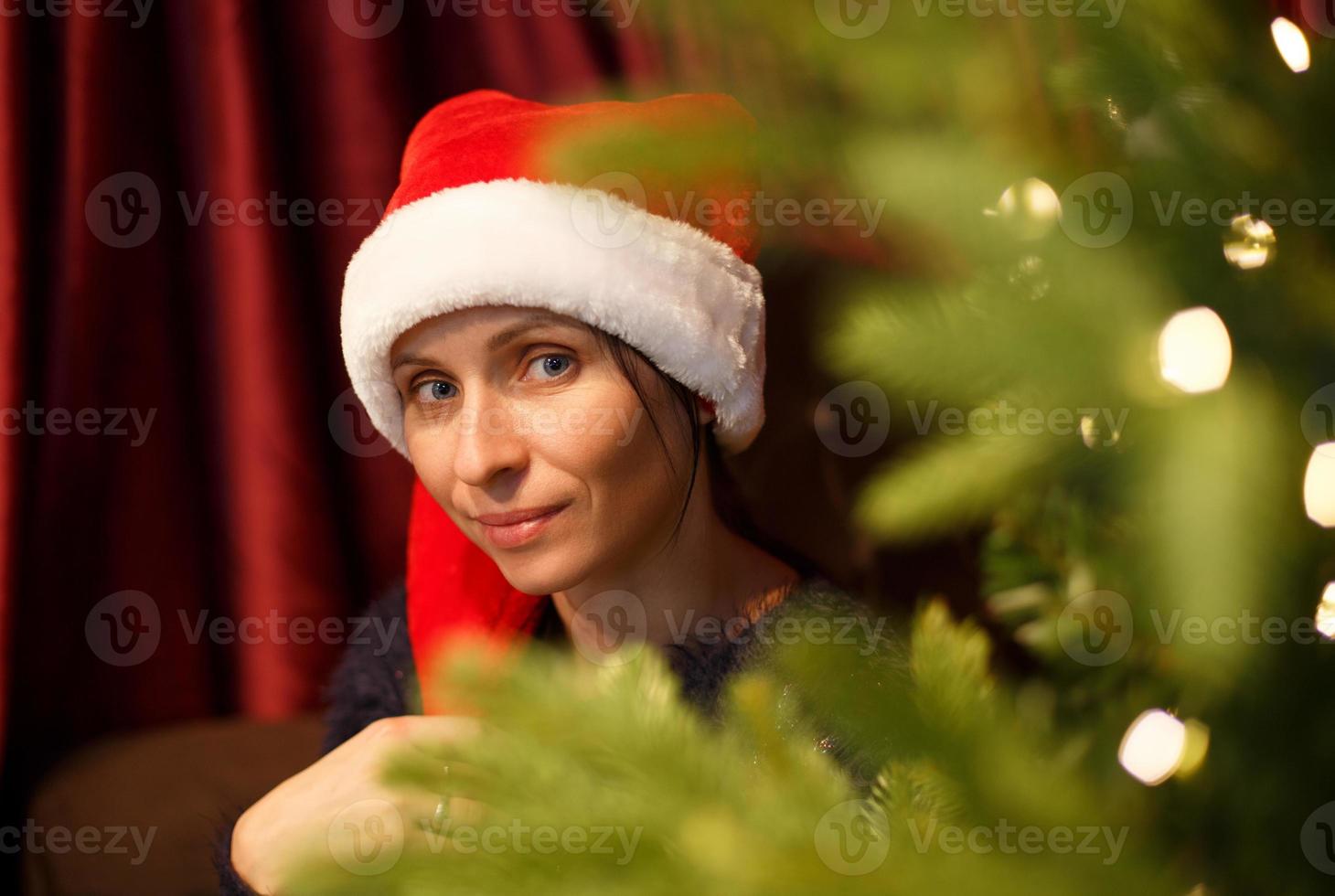 ritratto di una donna carina con un cappello di Babbo Natale vicino all'albero di natale foto