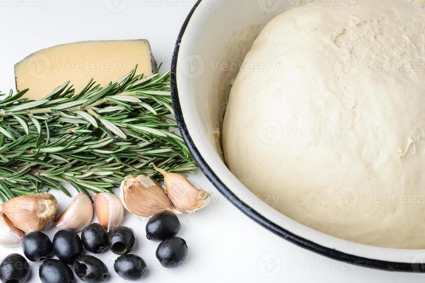 pasta per pizza in una ciotola, rosmarino, olive e formaggio su fondo bianco foto