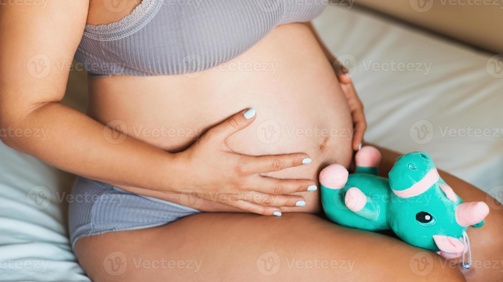 primo piano del ventre di una donna incinta con un peluche. il concetto di gravidanza, genitorialità, preparazione e attesa foto