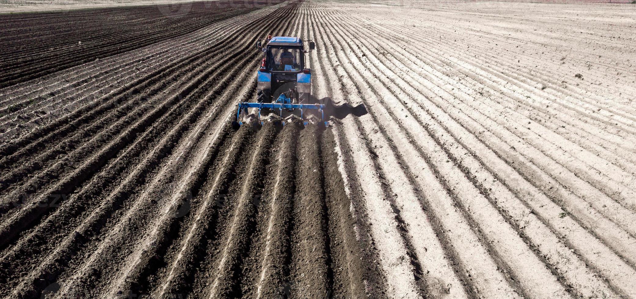 il trattore ara il campo nella vista posteriore della primavera foto