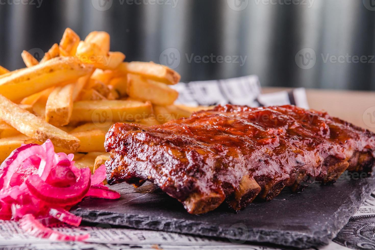 vista ravvicinata di costolette barbecue alla griglia con patatine fritte servite e pronte da mangiare foto