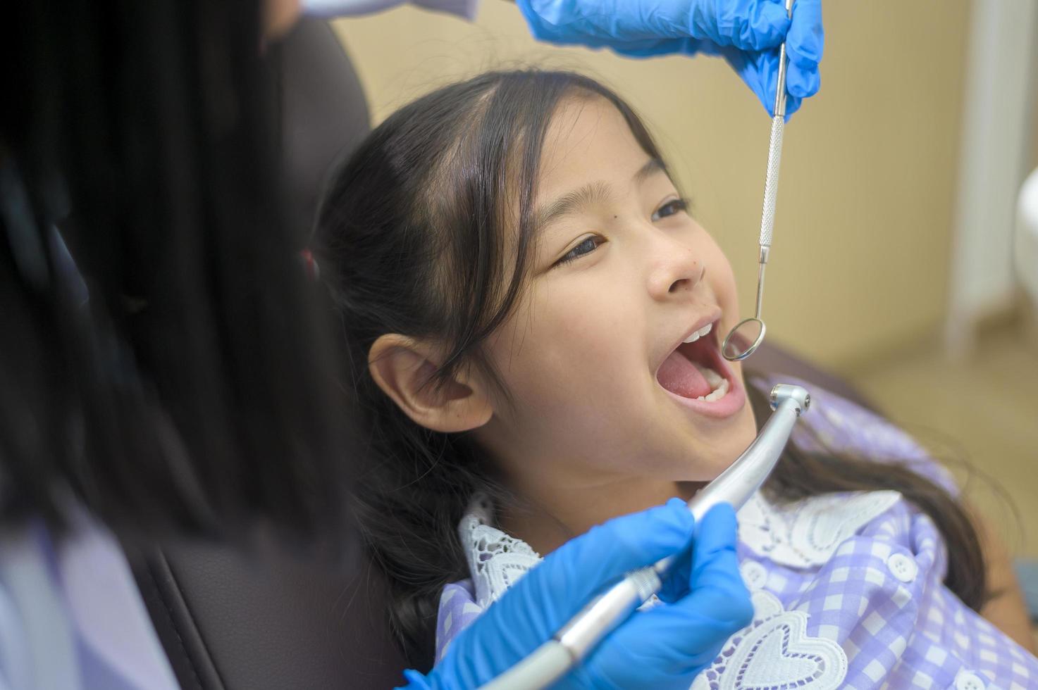 una piccola ragazza carina che ha i denti esaminati dal dentista in clinica dentale, controllo dei denti e concetto di denti sani foto