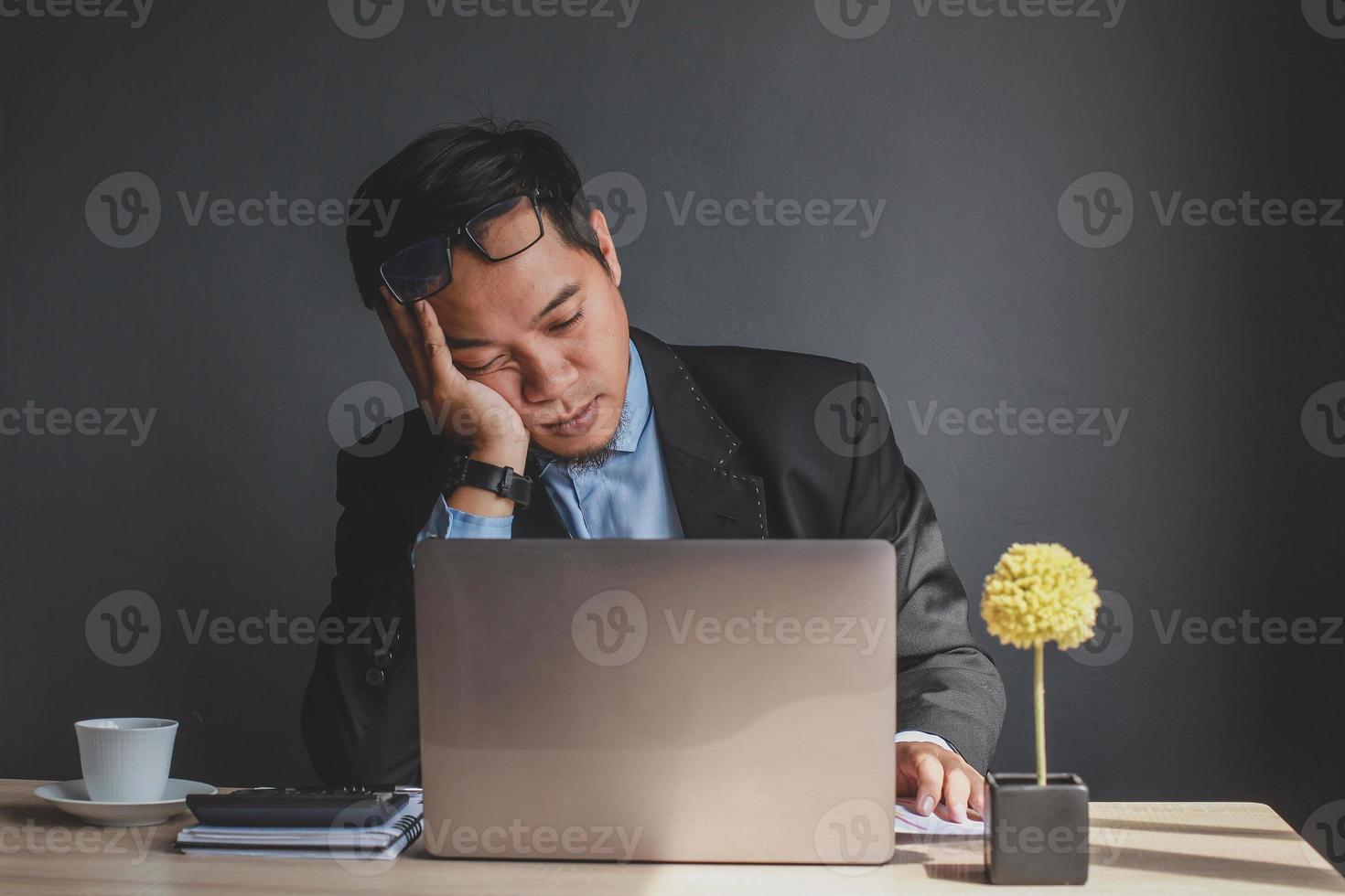 uomo d'affari asiatico che si addormenta alla scrivania dell'ufficio con gli occhi chiusi, giovane oberato di lavoro, lavoratore demotivato che dorme sul posto di lavoro, noioso del lavoro di routine foto