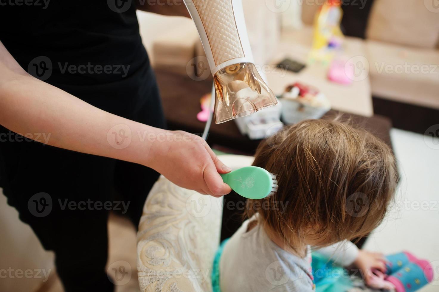 mamma con la figlia del bambino che fanno insieme la routine quotidiana. la madre sta spazzolando e asciugando i capelli del bambino dopo la doccia. foto