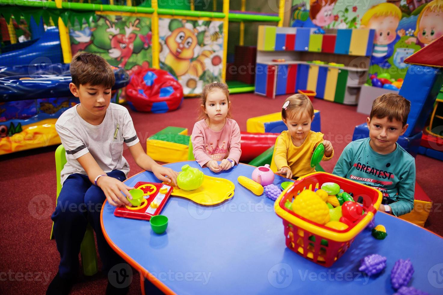quattro bambini che giocano nel centro giochi al coperto. stanza dei giochi dell'asilo o della scuola materna. seduto a tavola con frutti di plastica. foto
