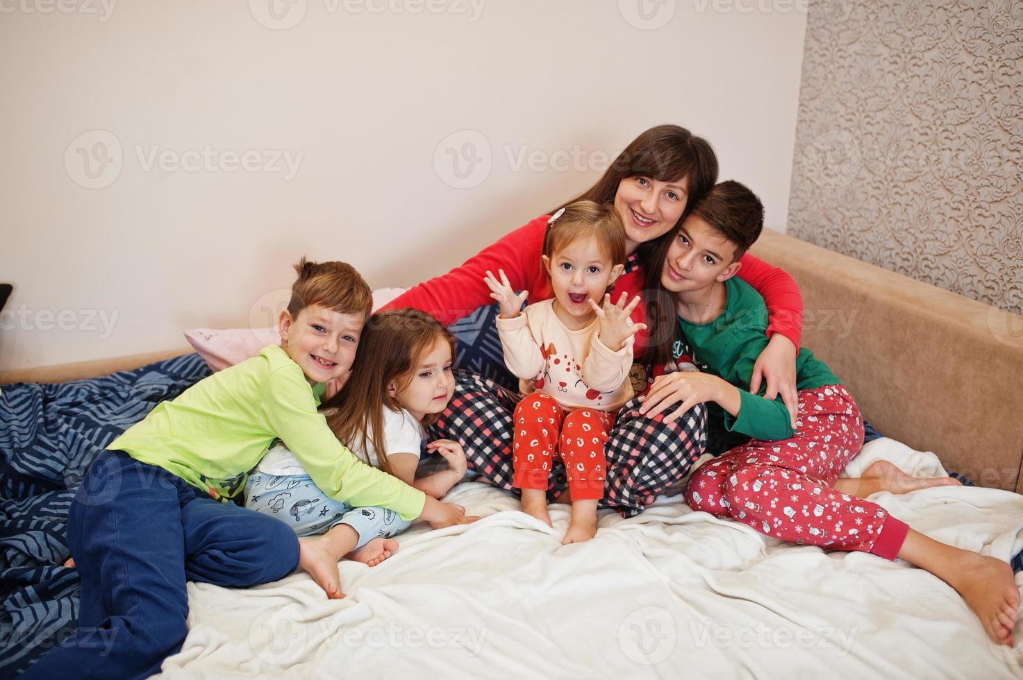 la grande famiglia felice si diverte insieme in camera da letto. concetto di mattina in famiglia numerosa. la madre con quattro bambini indossa il pigiama a letto a casa. foto