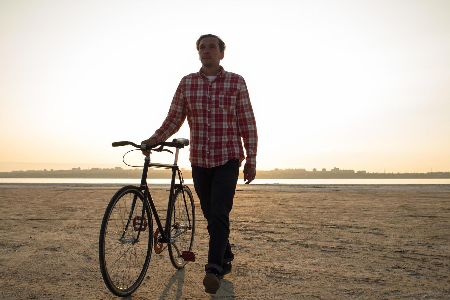 ciclista che cammina con la bici nera retrò durante l'alba nel deserto foto