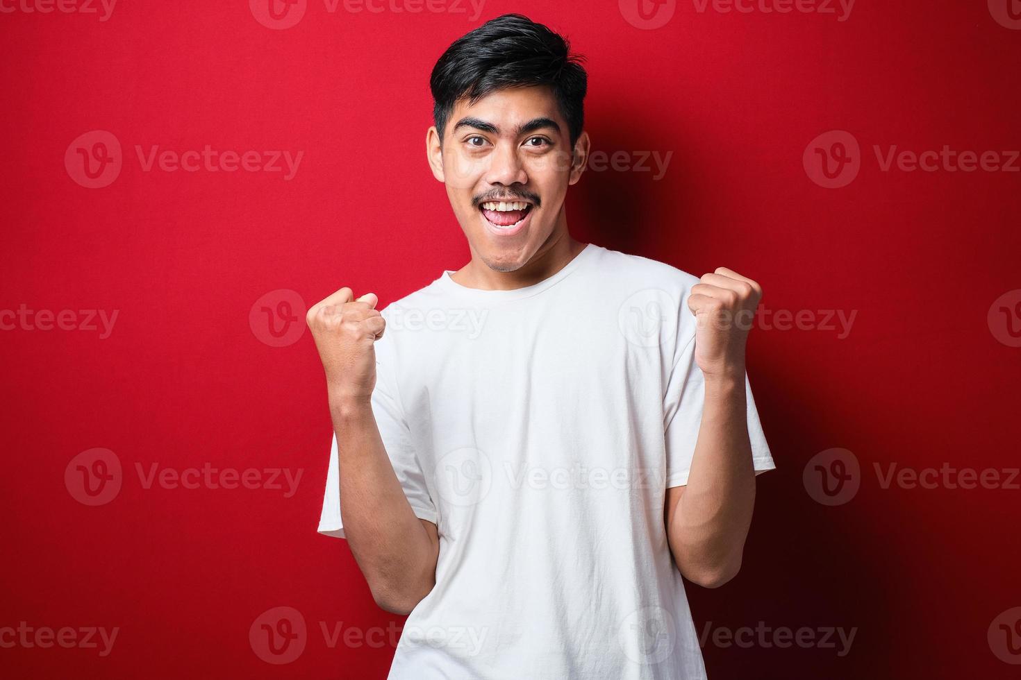 giovane bell'uomo che indossa una t-shirt bianca in piedi molto felice ed eccitato facendo il gesto del vincitore con le braccia alzate, sorridente e urlando per il successo. foto